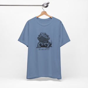 Before Coffee Bearded Dragon Blue t-shirt with a graphic design of a bearded dragon on a hanger against a white background