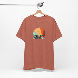 Brown t-shirt with colorful design and 'Full of Possibility' text on a hanger against a white background