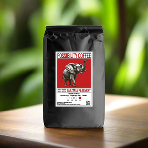 A black bag of Possibility Coffee Tanzania Peaberry Small Batch Roasted Single Origin on teak table with tropical plants in background