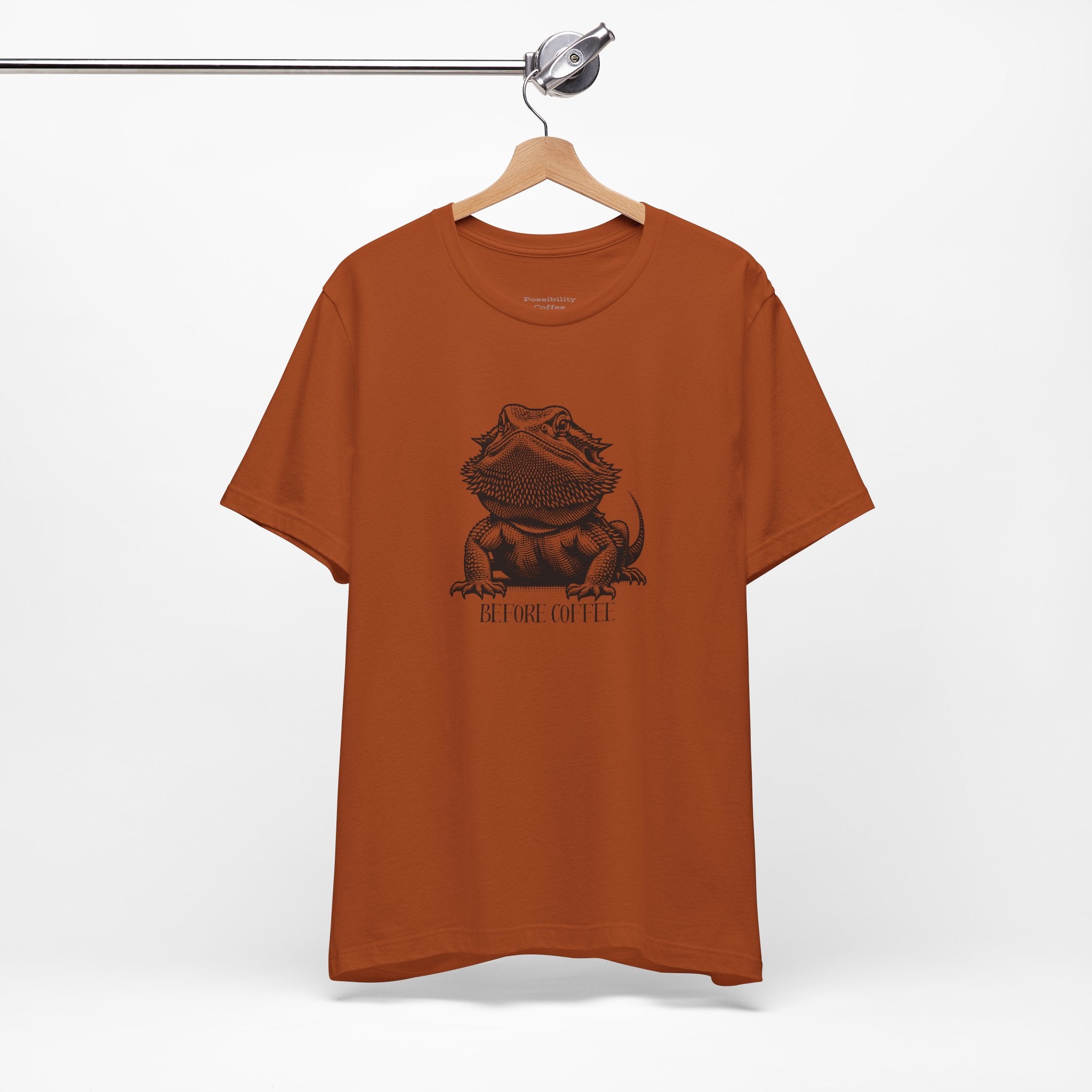 Before Coffee Bearded Dragon Orange  t-shirt with a graphic design on a hanger against a white background